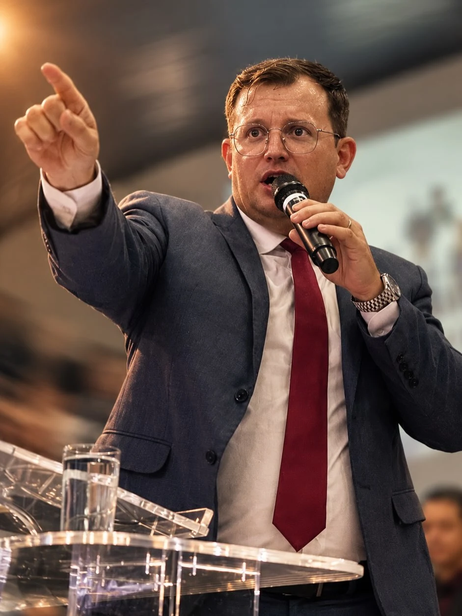 Pastor Cláudio Calais pregando ao microfone, com o braço erguido